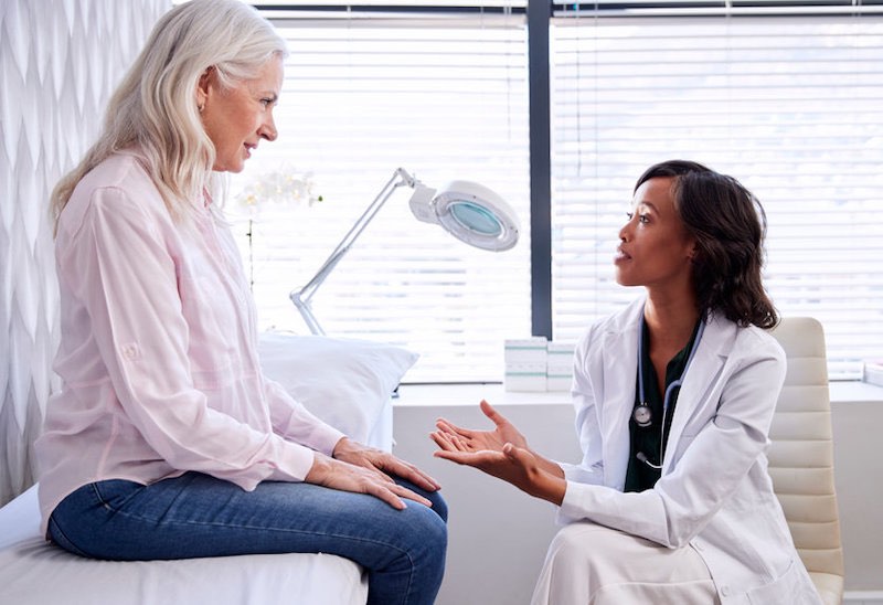 Mature Woman In Consultation With Female Doctor Sitting On Examination Couch In Office Mature Woman In Consultation With Female Doctor Sitting On Examination Couch In Office