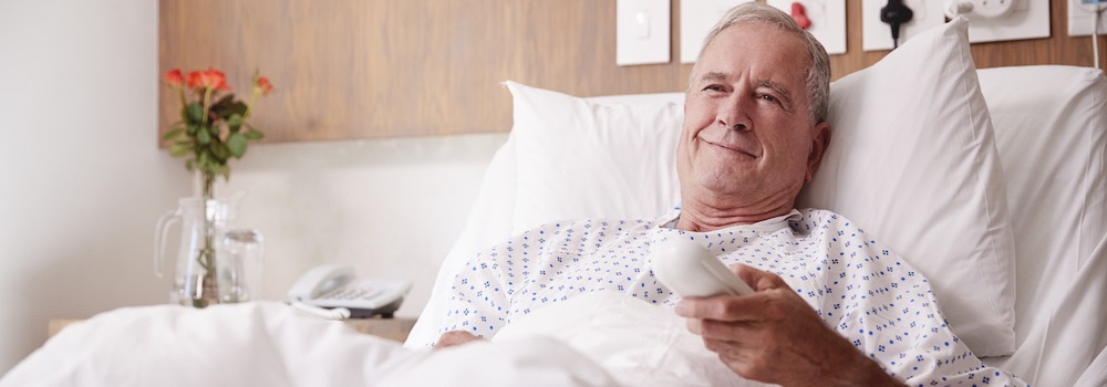 Male Senior Patient Lying In Hospital Bed Watching Television Male Senior Patient Lying In Hospital Bed Watching Television