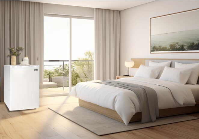 Modern hotel guest suite featuring a neatly styled bed and a compact Magic Chef mini fridge, ideal for hospitality and extended-stay comfort.